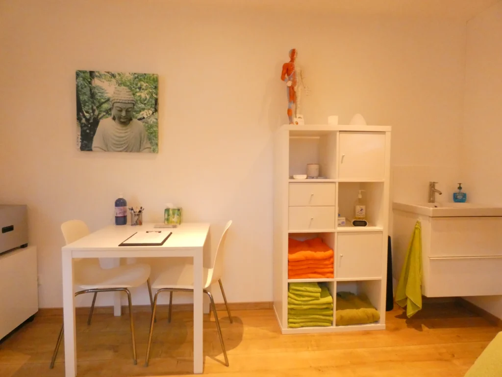 Tafel voor het intakegesprek met kast, handdoeken en wastafel in de praktijk